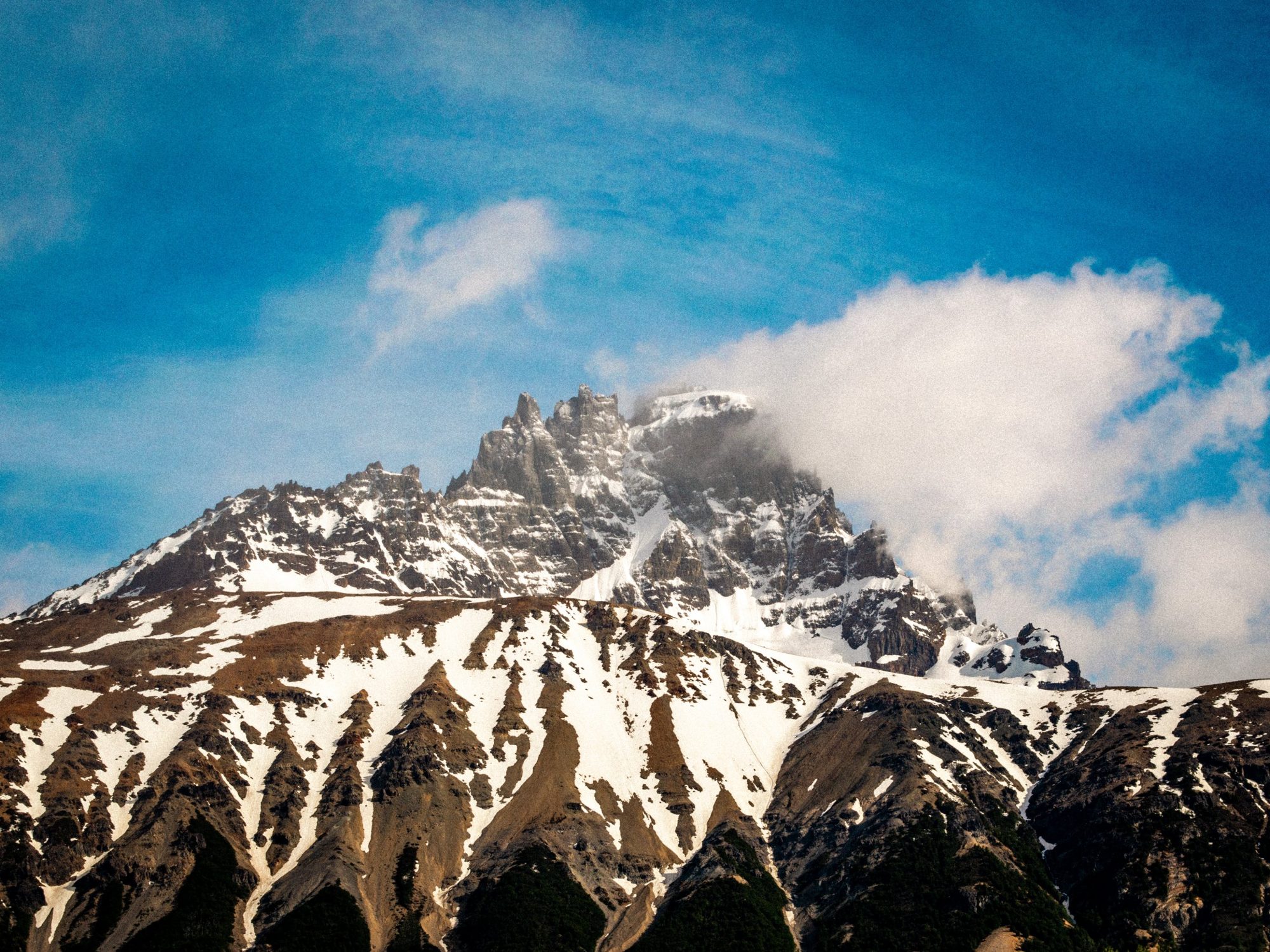 Cerro de cumbres rocosas nevadas con una nube en la cima