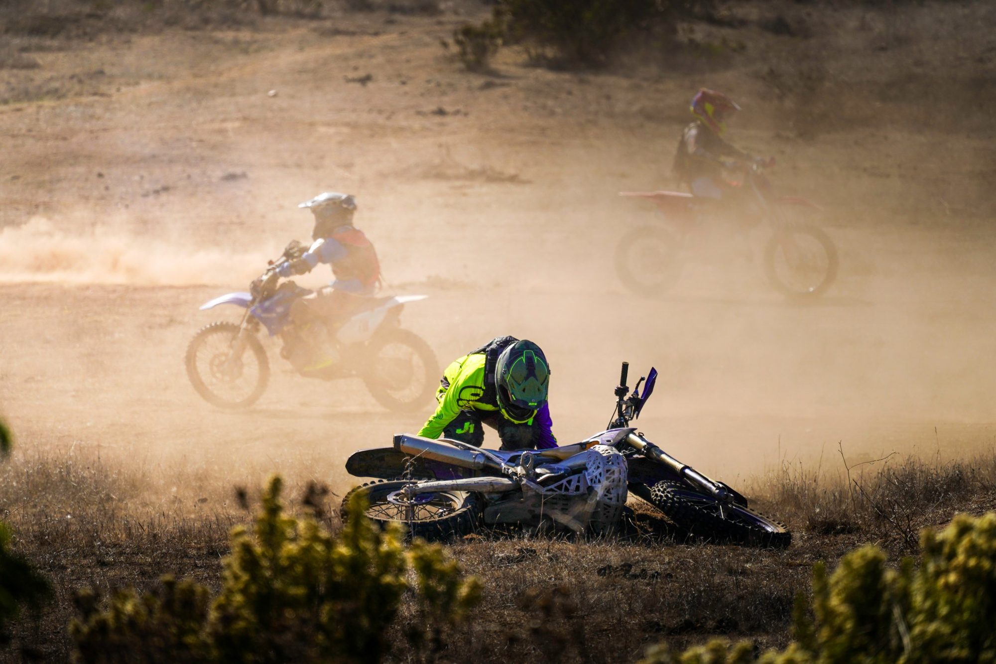 Piloto de motocross levantando su moto caída en medio del polvo