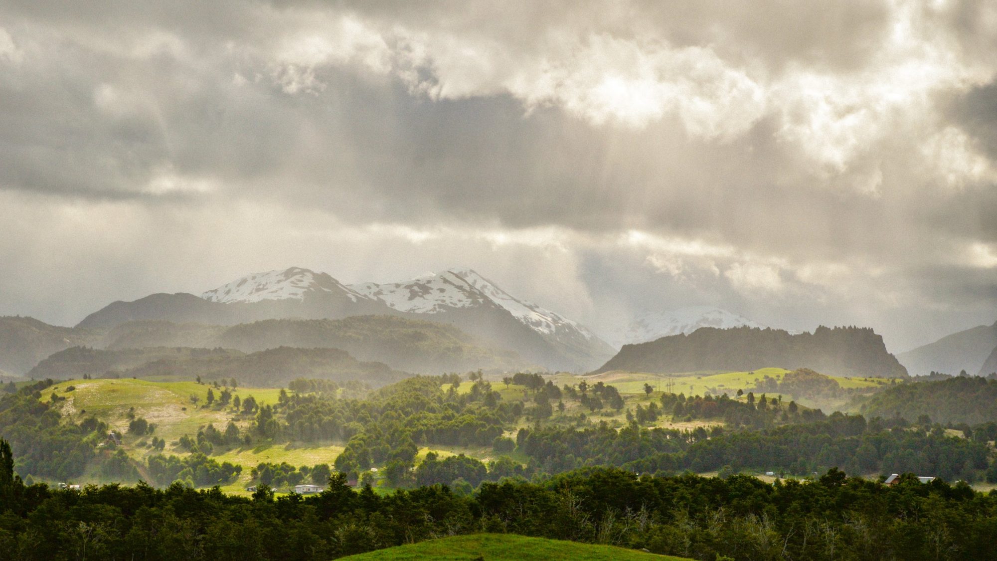 Valle verde con montañas nevadas bajo nubes de tormenta